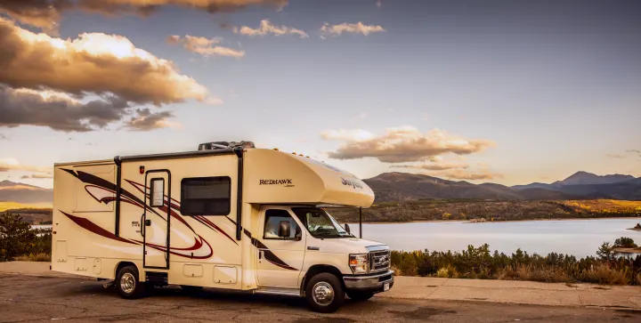 An RV rental (Jayco Redhawk) parked at a scenic lakeside viewpoint with mountains and a golden sunset sky.. Jayco Redhawk 2016