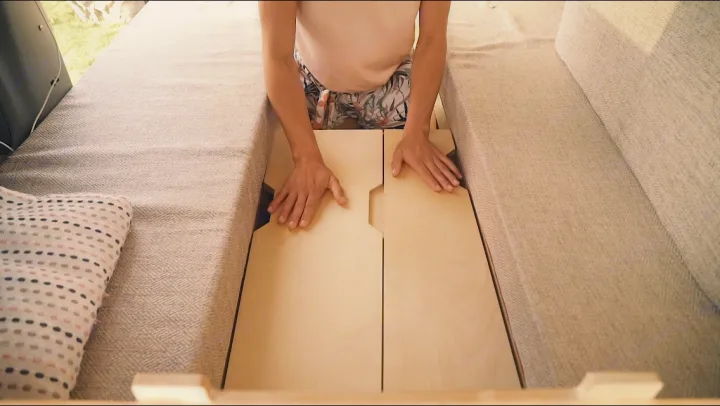 RV rental interior: A person adjusts wooden panels, converting seating into a bed or accessing storage, a smart space-saving design.. Toyota Noah 2005