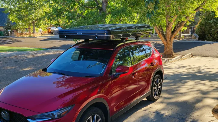 Red SUV with a sleek black hard-shell rooftop tent, ready for **rv rental** camping trips.. Mazda Campervan 2018
