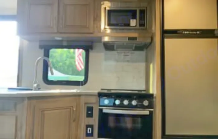 An RV rental kitchen, showing sink, microwave, stove/oven, and fridge. A window reveals an American flag outside. Ready for your travels.. Forest River Palomino Solaire 2021
