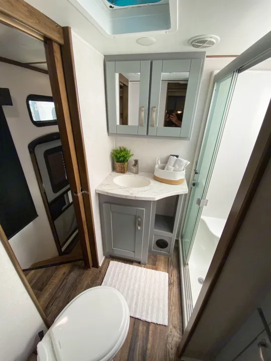 Clean RV rental bathroom with modern gray vanity, white sink, toilet, and glass shower. Functional travel space.. Keystone Fuzion 2020
