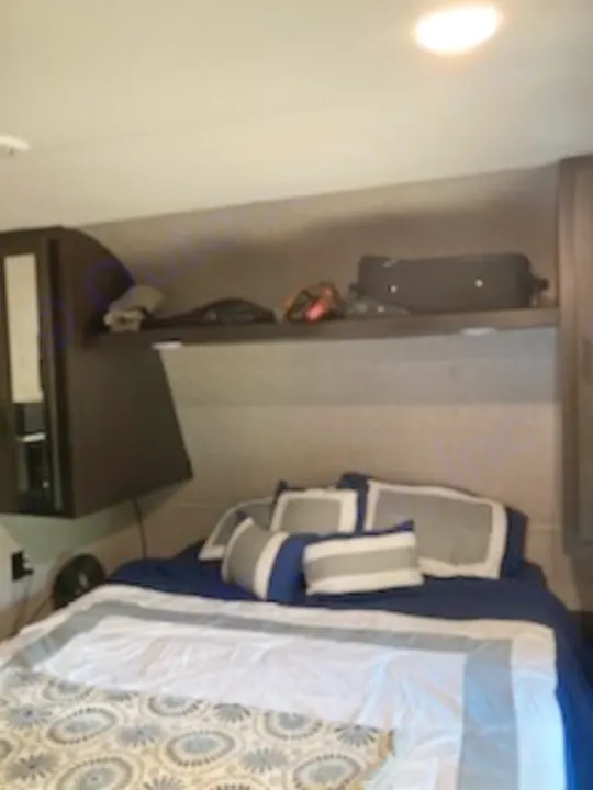 Inside an RV rental: a compact bedroom with a comfortable bed, pillows, and convenient overhead storage shelf.. Jayco Jay Flight 2022