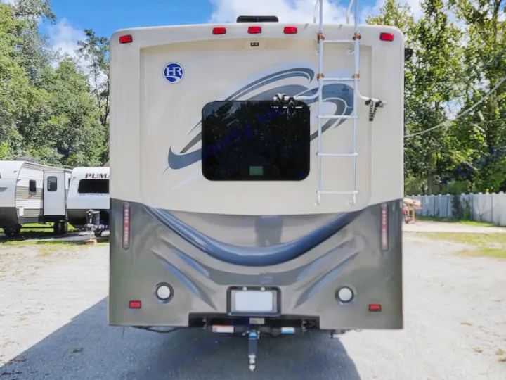 Rear view of a beige & gray RV rental, parked outdoors. A full-size motorhome with a ladder, rear window, and hitch receiver.. Holiday Rambler Admiral 2016