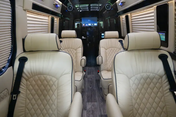 Luxurious RV rental interior with cream-colored, quilted leather seats, window blinds, and entertainment screens in the passenger cabin.. Ultimate Toys Ultimate Traveler 2022