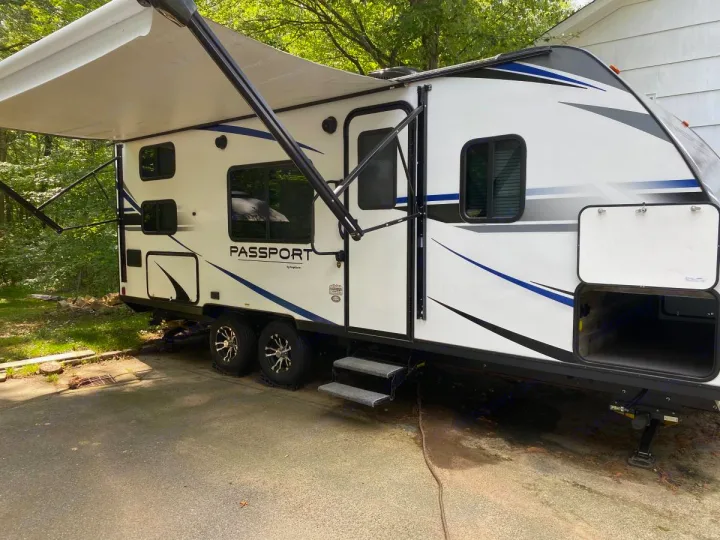 White Passport travel trailer RV rental with awning extended, parked on asphalt. Open storage compartment visible.. Other Passport 2020