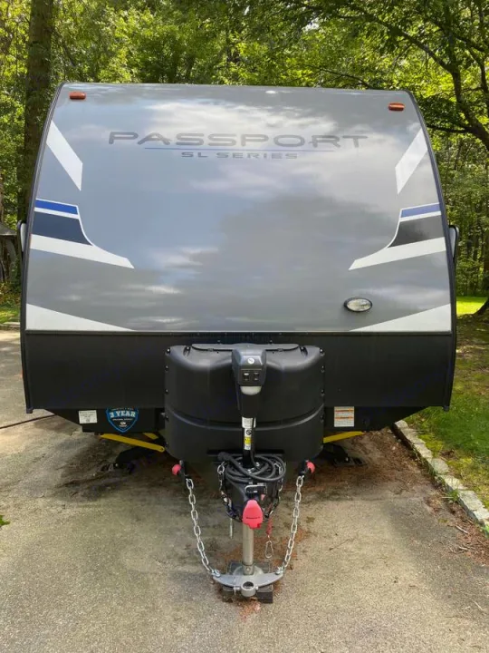 Front view of a grey Passport SL Series travel trailer, ideal for an RV rental adventure. Parked outdoors with hitch visible.. Other Passport 2020