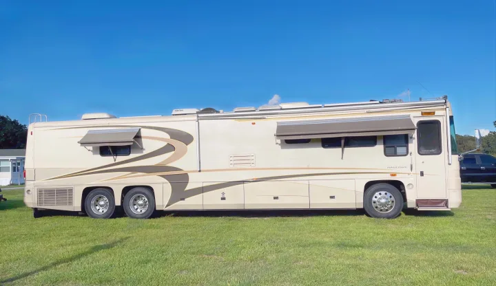 This large, beige Class A RV (Private Coach) on grass awaits your next rv rental adventure under a blue sky.. Foretravel U-320 2001
