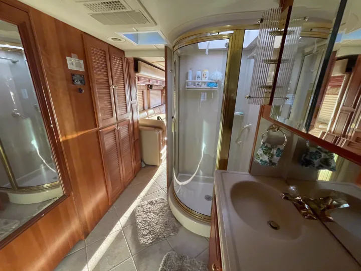 RV rental interior: A compact bathroom with curved shower, sink, and wood cabinets, extending to the main living area.. Foretravel U-320 2001