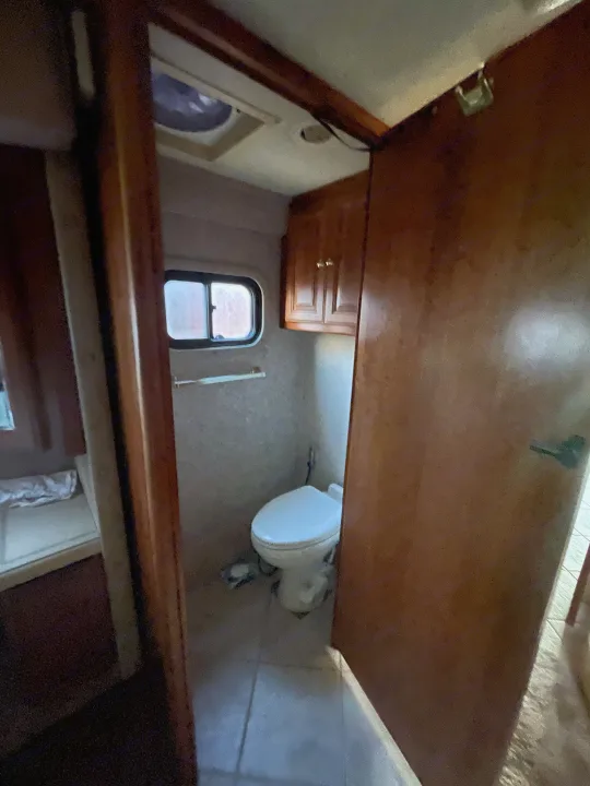 Compact RV rental bathroom with toilet, small window, and overhead cabinets, providing essential amenities for your travels.. Foretravel U-320 2001