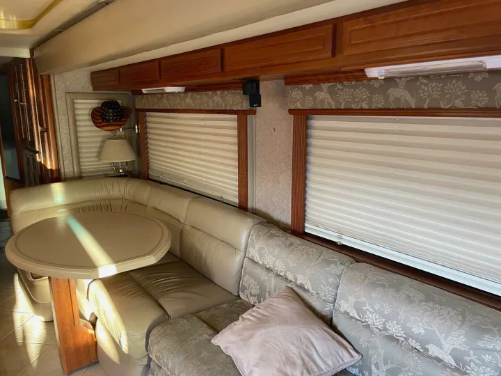 RV rental interior with cream leatherette and patterned sofa, dining area, windows, and wood cabinetry.. Foretravel U-320 2001