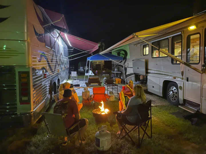 Nighttime RV camping: Friends enjoy a warm campfire at an RV campsite between two motorhomes, ideal for an RV rental experience.. Foretravel U-320 2001