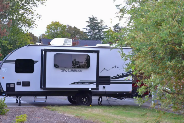 A white Wolf Pup Black Label travel trailer RV rental, with mountain graphics, parked on a campsite amidst trees.. Forest River Cherokee Wolf Pup 2020