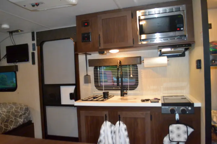 RV rental kitchen & sleeping area: modern design with microwave, sink, stovetop, cabinets, and a glimpse of a bed.. Forest River Cherokee Wolf Pup 2020