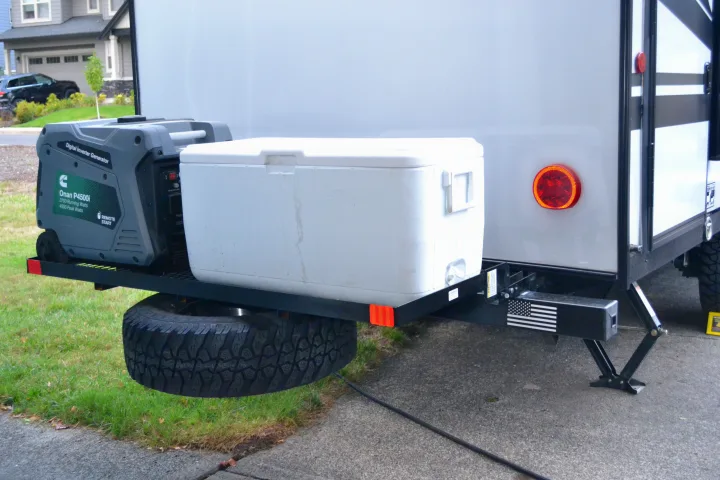 Rear of an RV rental: a gray generator & white cooler sit on a cargo rack above a spare tire, with stabilizer jacks.. Forest River Cherokee Wolf Pup 2020