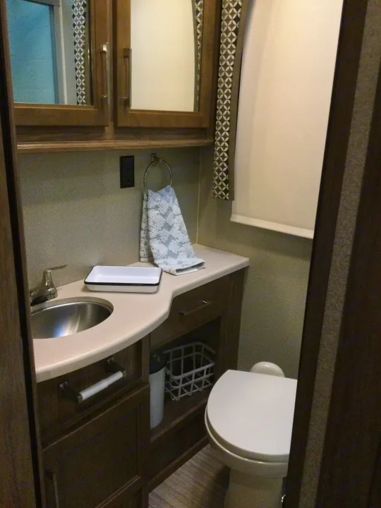 Compact RV rental bathroom with sink, faucet, toilet, and storage cabinets, offering essential amenities.. Jayco Greyhawk 2018