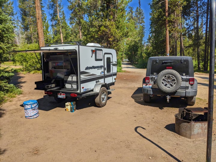An RV rental trailer and Jeep at a campsite. Enjoying outdoor cooking from the Jay Feather Micro's rear galley.. Jayco Jay Feather Micro 12SRK 2021
