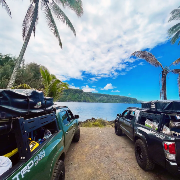 Two overland trucks with rooftop tents by a scenic bay. Perfect for your next RV rental adventure!. Toyota Tacoma 2021