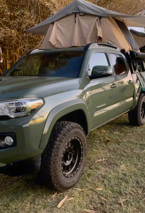 A rugged green Toyota Tacoma pickup with a rooftop tent sits on grass, showcasing an overland RV rental for your next camping trip.. Toyota Tacoma 2021