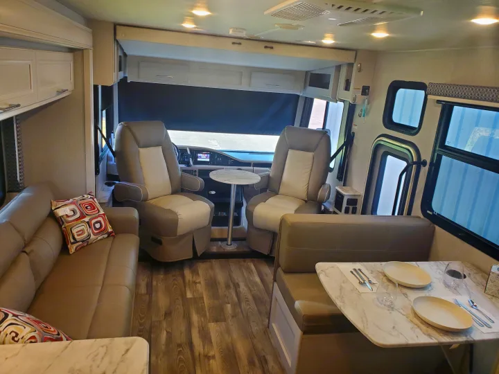 Inside a spacious RV rental: Modern interior featuring swivel seats, a sofa, and a cozy dinette set for dining.. Holiday Rambler Admiral 2022