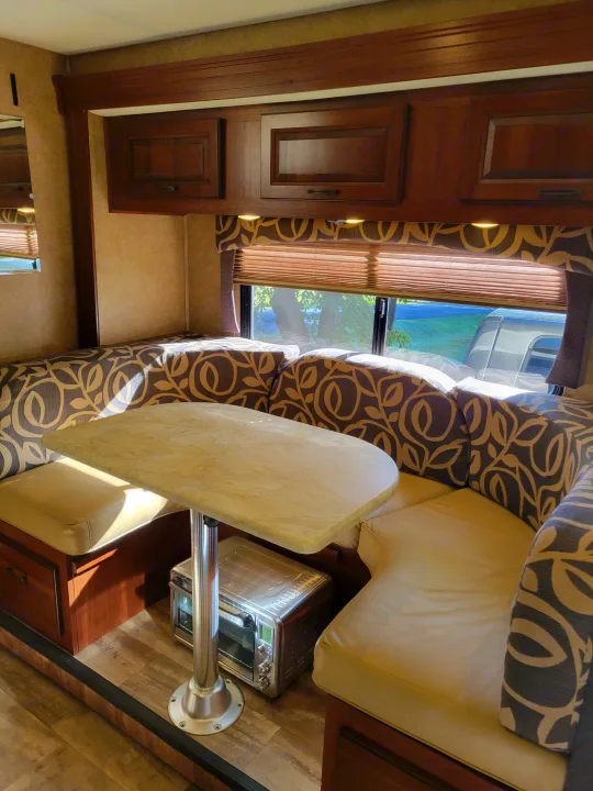 Cozy RV rental dinette with U-shaped seating, patterned cushions, a light table, storage, and window with blinds.. Forest River Forester 3011DS 2015