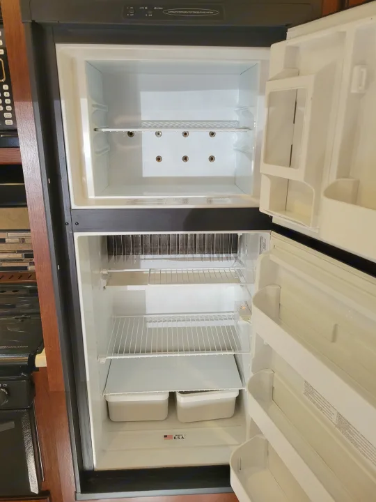 An empty, clean refrigerator is open in an RV rental, showing shelves, freezer, and door storage, ready. Forest River Forester 3011DS 2015