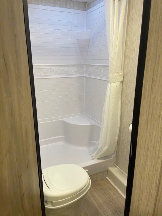 Inside an RV rental bathroom: a compact white shower with curtain and toilet on wood-look flooring.. Palomino Puma 2022