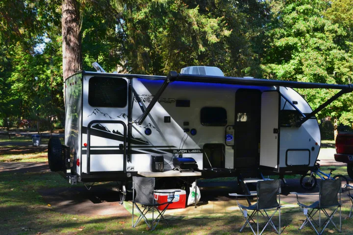 Relax at your next RV rental: a modern travel trailer campsite with an awning, outdoor chairs, and cooking setup.. Forest River Cherokee Wolf Pup 2020