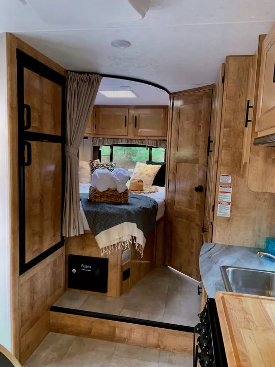 Cozy RV rental interior with bed, kitchen, and warm wood tones, perfect for travel adventures.. Coachmen Leprechaun 2021