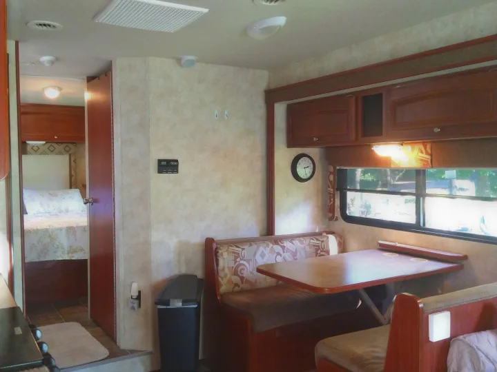 Inside an RV rental: a spacious dinette area with built-in seating, overhead storage, and a peek into the bedroom.. Winnebago Access 2011