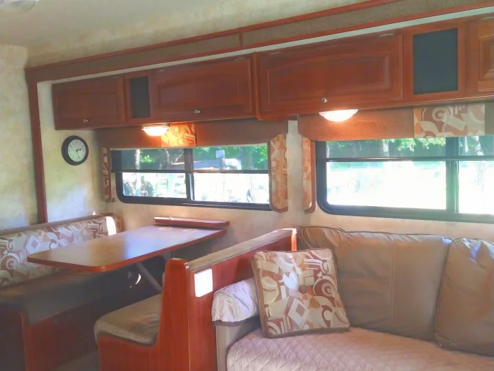Cozy RV rental interior with a dinette, sofa, and overhead cabinets, offering comfort for travel.. Winnebago Access 2011