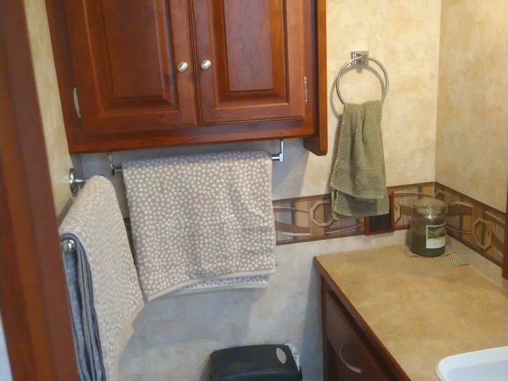 Compact RV rental bathroom with dark wood cabinets, a counter, and towels for comfort and convenience.. Winnebago Access 2011