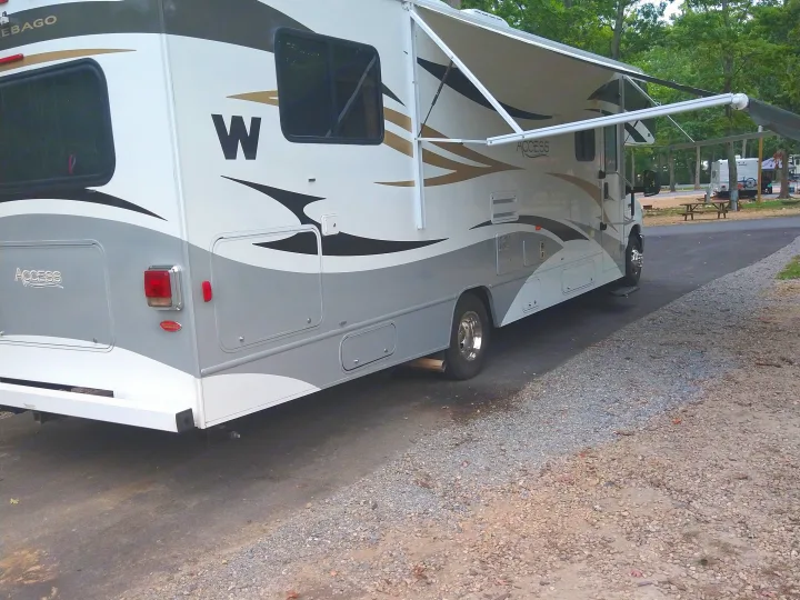 RV rental: A white and gray Winnebago Access motorhome with its awning extended, parked on asphalt at a campground.. Winnebago Access 2011