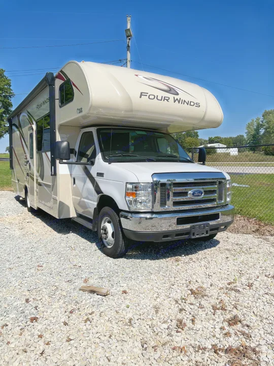 White and tan Four Winds Class C RV rental, a motorhome, parked on gravel under a clear blue sky.. THOR FOUR WINDS 26 B 2021