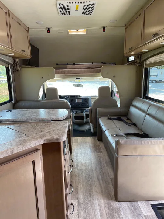 Inside an RV rental: a bright, spacious interior featuring a kitchen counter, comfy sofa with seatbelts, and front driver's cab.. THOR FOUR WINDS 26 B 2021
