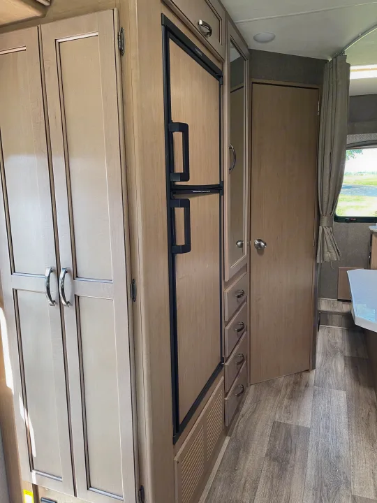 RV rental interior features light wood cabinets, a built-in refrigerator, and wood-look flooring, with a partial view of a closet and window.. THOR FOUR WINDS 26 B 2021