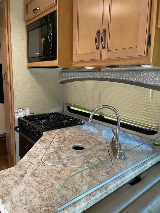 Compact RV rental kitchen featuring a microwave, stove, covered sink, and light-toned cabinets.. THOR FOUR WINDS 26 B 2021