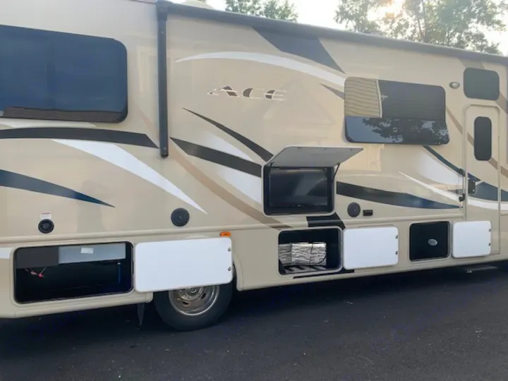View of an RV rental: beige motorhome with open external storage and an outdoor TV visible. Ready for adventure!. Thor Motor Coach A.C.E 2017