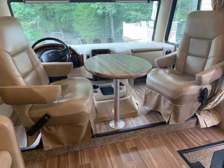 RV rental interior: two comfortable tan captain's chairs, a small round table, and laminate wood flooring visible.. Thor Motor Coach A.C.E 2017