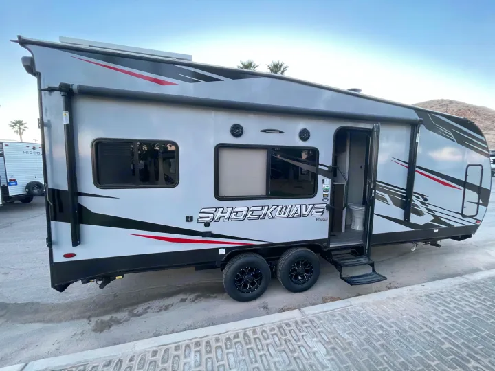 This gray Shockwave toy hauler travel trailer, an ideal RV rental option, is parked outdoors, ready for your next adventure.. Forest River Shockwave 2021