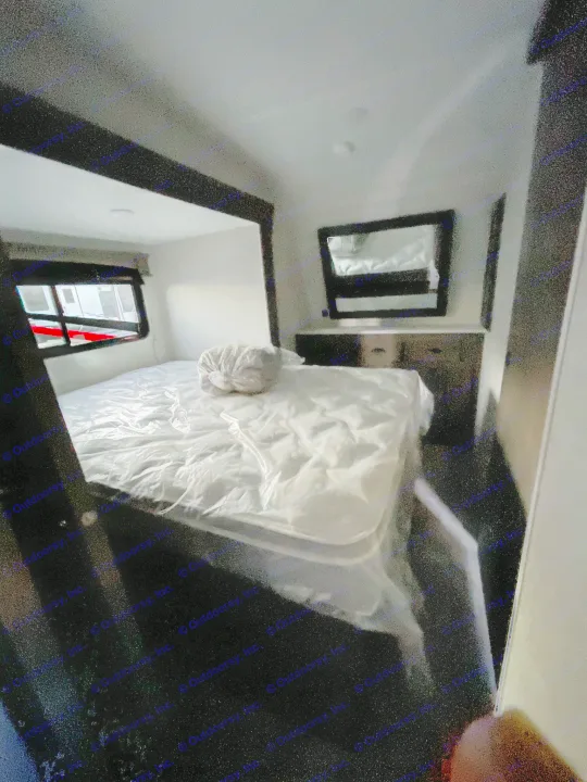 Clean RV rental bedroom featuring a plastic-wrapped mattress, dresser with mirror, and window view.. Forest River Shockwave 2021