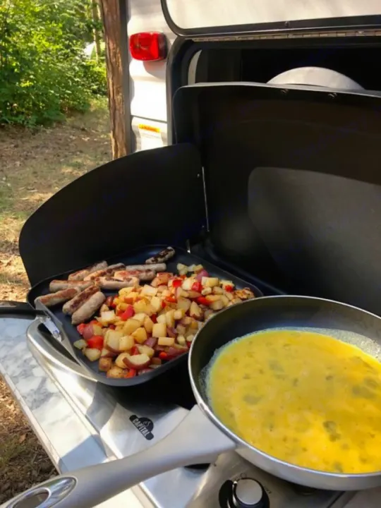Outdoor RV rental breakfast: sausages & potatoes on griddle, eggs in pan. Perfect camping meal!. Dutchman Aspen Trail 2022