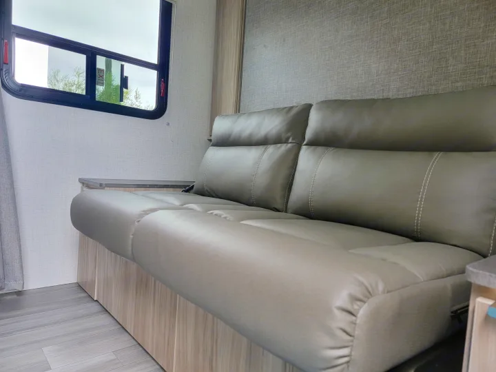 Comfortable grey leather sofa in an RV rental, featuring a textured interior wall, laminate floor, and window with an 'EXIT' sign.. Winnebago Micro Minnie 2021