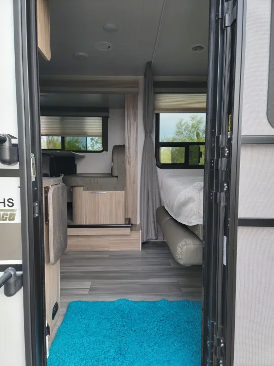 Looking inside a modern RV rental, featuring a compact living area with bed, cabinetry, and contrasting flooring.. Winnebago Micro Minnie 2021