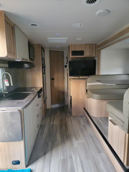 Modern RV rental interior showing a compact kitchen, dining area, and entertainment setup. Light wood and gray tones create a spacious feel.. Winnebago Micro Minnie 2021