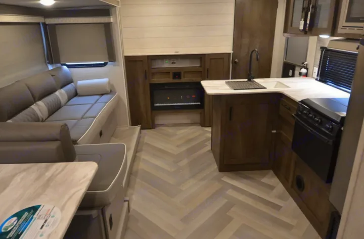 Bright, modern RV rental interior featuring a full kitchen, comfortable sofa/dinette, and electric fireplace. Ideal for travel.. Forest River Wildwood X-Lite 2022