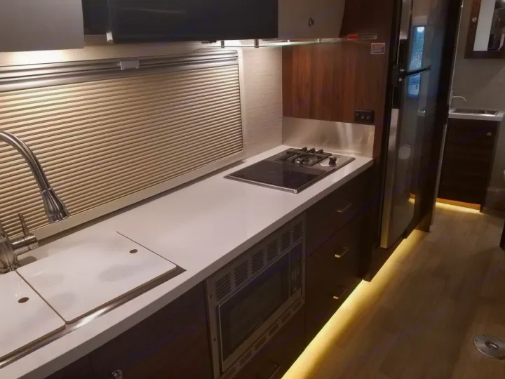 RV rental galley: modern kitchen with sink, stovetop, microwave & under-cabinet lighting illuminating dark wood.. Winnebago View 2022