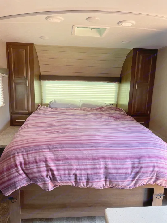 Experience comfort in this RV rental bedroom. Features a cozy striped bed, side cabinets, and a bright window with blinds.. Forest River Rockwood Mini Lite 2020