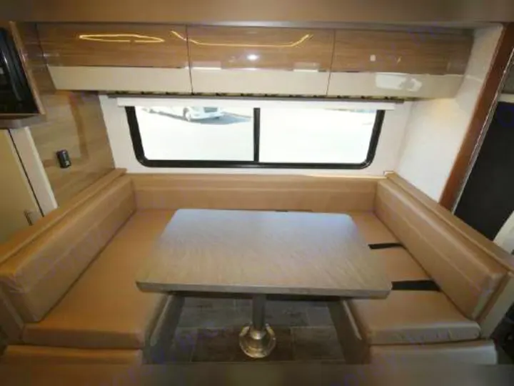 Spacious RV rental dinette with light-colored booth seating, a central table, and a large window view.. Winnebago View 2018