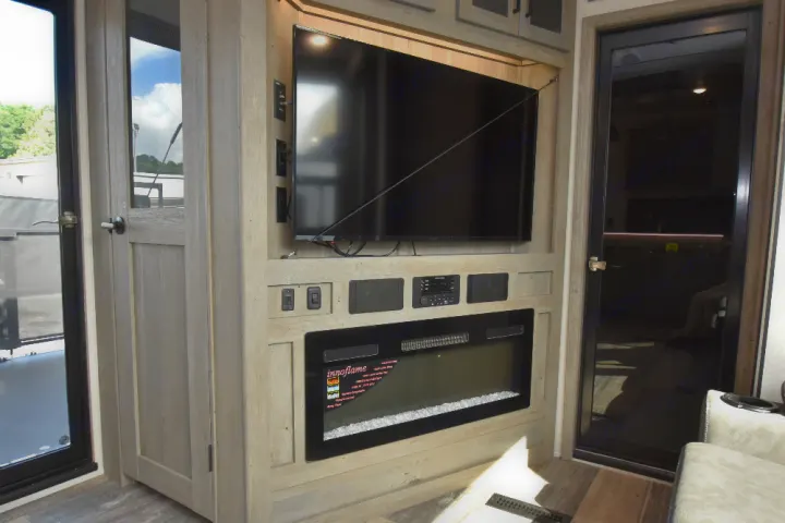 RV rental entertainment center with a large TV, fireplace, and integrated audio system, set in light wood paneling.. Keystone Raptor 2025