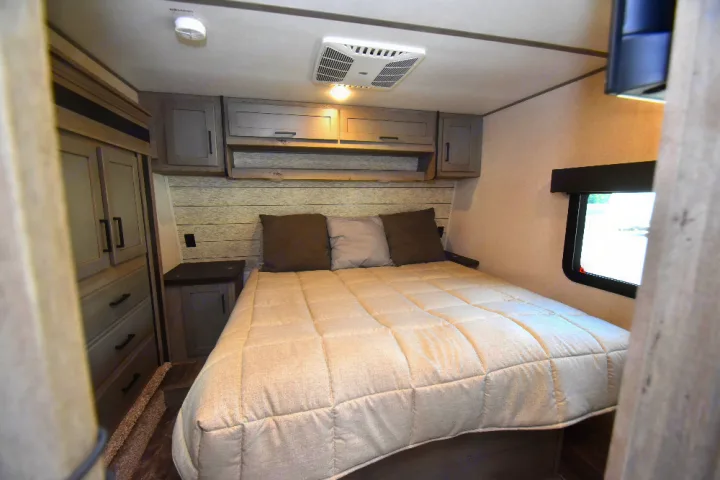 Comfortable RV rental bedroom with a queen bed, overhead cabinets, wardrobe, AC unit, and window.. Keystone Raptor 2025